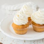 Three vanilla frosted cupcakes on a white plate and table