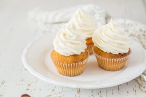 Three vanilla frosted cupcakes on a white plate and table